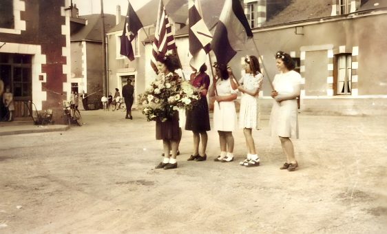 Des jeunes femmes tiennent un drapeau et des fleurs pour la fin de la seconde guerre mondiale.